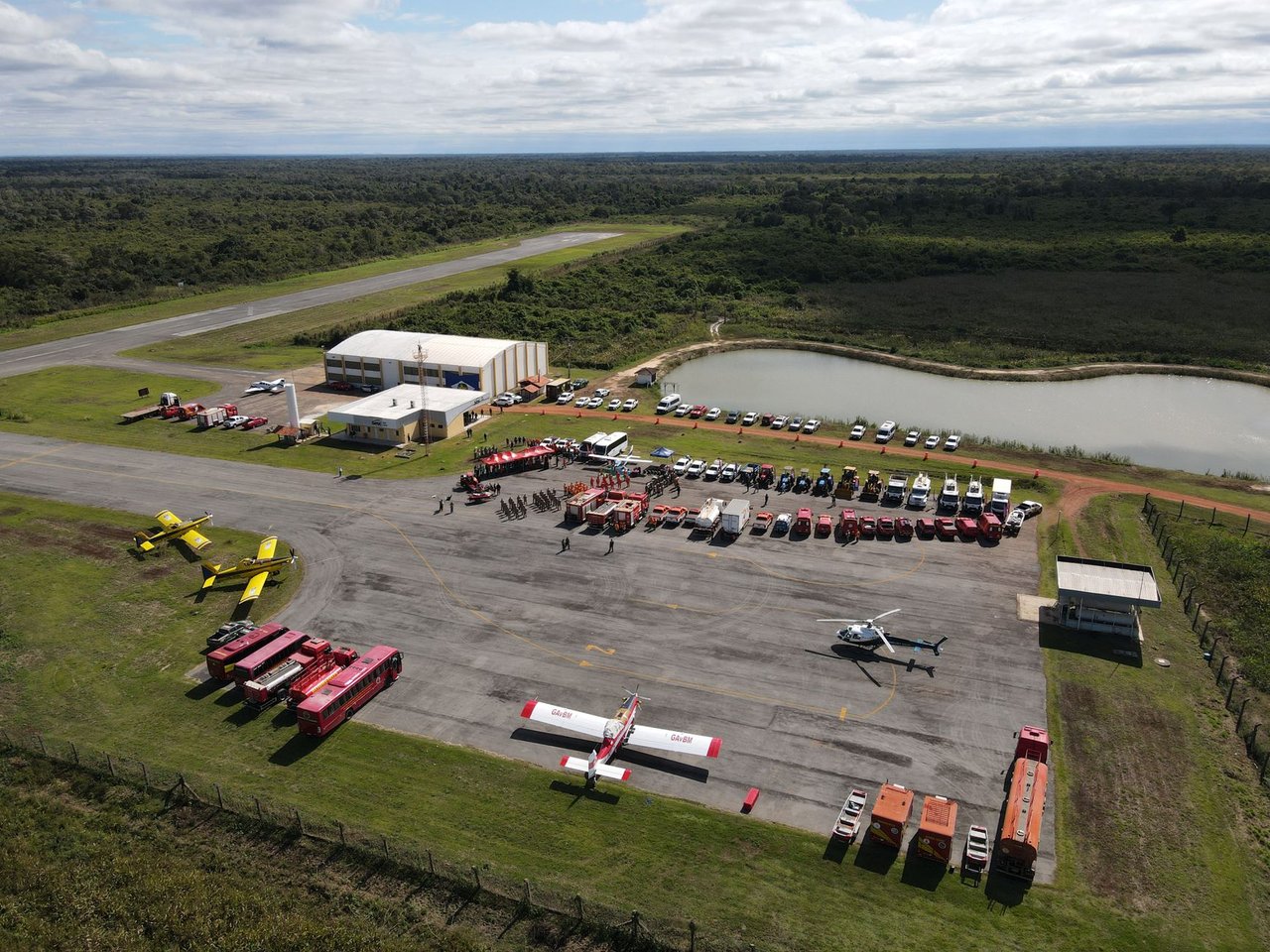 Vista aérea de uma base de combate a incêndios florestais, com caminhões, helicópteros e aviões preparados para a operação.