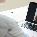Mulher participa de uma videoconferência usando um laptop em um ambiente de trabalho.