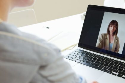 Mulher participa de uma videoconferência usando um laptop em um ambiente de trabalho.