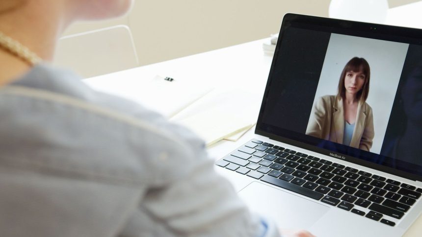 Mulher participa de uma videoconferência usando um laptop em um ambiente de trabalho.