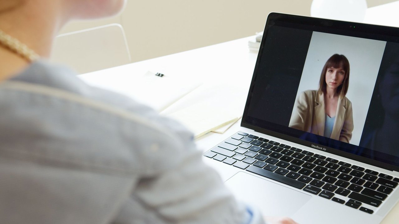 Mulher participa de uma videoconferência usando um laptop em um ambiente de trabalho.