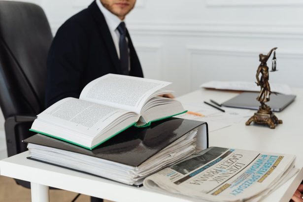 Advogado sentado à secretária, rodeado de livros jurídicos, documentos e um jornal.
